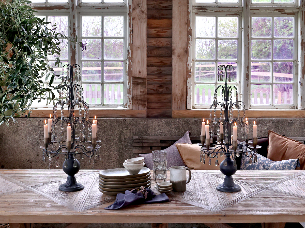 "Dekoracje vintage nadają wnętrzu niepowtarzalny klimat – dwa stylowe świeczniki z kryształkami i zapalonymi świecami na drewnianym stole tworzą elegancką i przytulną aranżację.