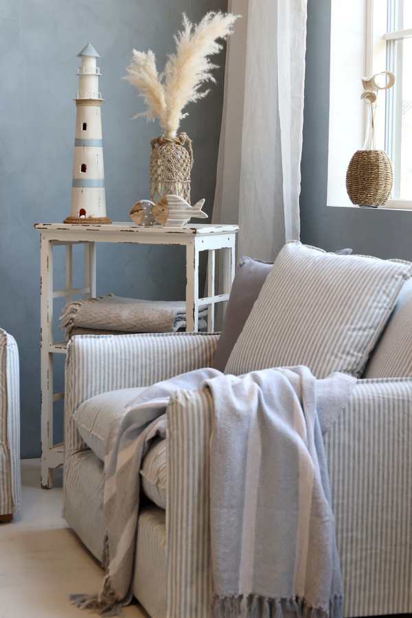 Kącik w stylu nadmorskim z fotelami w biało-niebieskie pasy, dekoracyjną latarnią, koszami z wikliny i dodatkami marynistycznymi przy oknie.
